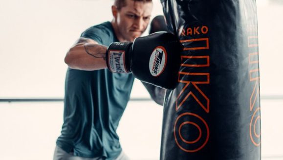 An adult male boxer in a gym actively punching a heavy bag for fitness training.